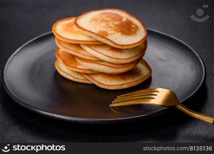 Delicious fresh pancakes on a black plate against a dark concrete background. Making a delicious breakfast. Delicious fresh pancakes on a black plate against a dark concrete background