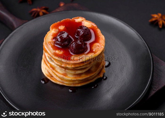 Delicious fresh pancakes with berry jam on a black ceramic plate on a dark concrete background