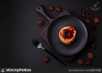 Delicious fresh pancakes with berry jam on a black ceramic plate on a dark concrete background