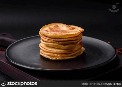 Delicious fresh pancakes with berry jam on a black ceramic plate on a dark concrete background