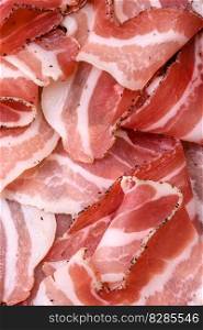 Delicious fresh pancetta with sa<and sπces cut∫o thin slices on a dark concrete background