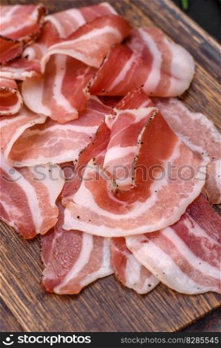Delicious fresh pancetta with salt and spices cut into thin slices on a dark concrete background