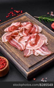 Delicious fresh pancetta with salt and spices cut into thin slices on a dark concrete background