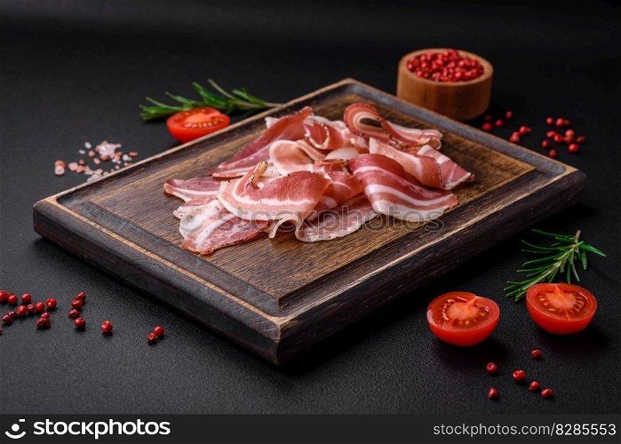 Delicious fresh pancetta with salt and spices cut into thin slices on a dark concrete background