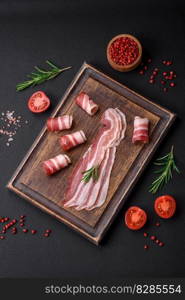 Delicious fresh pancetta with salt and spices cut into thin slices on a dark concrete background