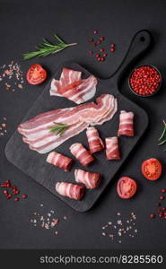 Delicious fresh pancetta with salt and spices cut into thin slices on a dark concrete background