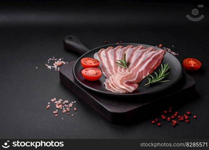 Delicious fresh pancetta with salt and spices cut into thin slices on a dark concrete background