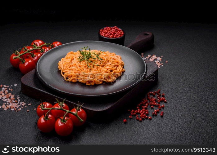 Delicious fresh pasta consisting of thin noodles, red pesto rosso sauce with salt, spices and herbs on a dark concrete background