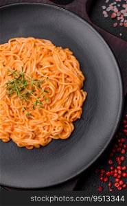 Delicious fresh pasta consisting of thin noodles, red pesto rosso sauce with salt, spices and herbs on a dark concrete background