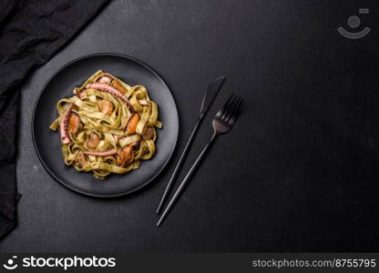 Delicious fresh pasta with pesto sauce and seafood on a black plate against a dark concrete background. Delicious fresh pasta with pesto sauce and seafood on a black plate