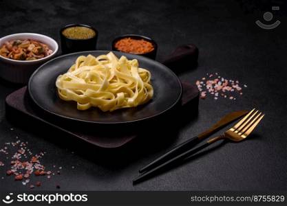 Delicious fresh pasta with pesto sauce and seafood on a black plate against a dark concrete background. Delicious fresh pasta with pesto sauce and seafood on a black plate