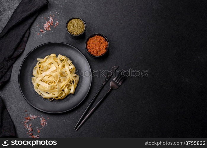 Delicious fresh pasta with pesto sauce and seafood on a black plate against a dark concrete background. Delicious fresh pasta with pesto sauce and seafood on a black plate