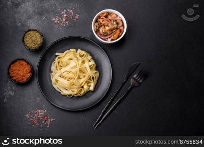 Delicious fresh pasta with pesto sauce and seafood on a black plate against a dark concrete background. Delicious fresh pasta with pesto sauce and seafood on a black plate