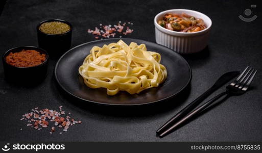 Delicious fresh pasta with pesto sauce and seafood on a black plate against a dark concrete background. Delicious fresh pasta with pesto sauce and seafood on a black plate