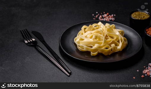 Delicious fresh pasta with pesto sauce and seafood on a black plate against a dark concrete background. Delicious fresh pasta with pesto sauce and seafood on a black plate