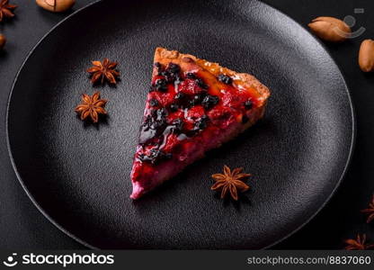 Delicious fresh pie with raspberries and other berries and cheese on a dark plate on a black background