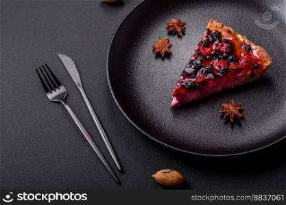 Delicious fresh pie with raspberries and other berries and cheese on a dark plate on a black background