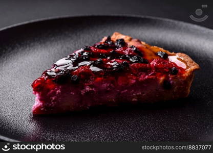 Delicious fresh pie with raspberries and other berries and cheese on a dark plate on a black background