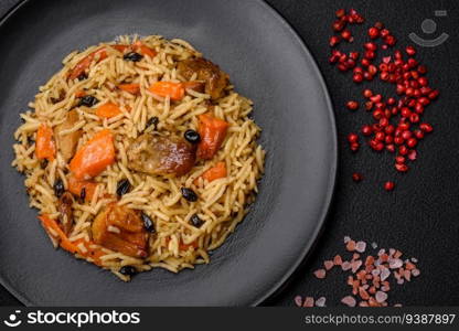 Delicious fresh pilaf with rice, carrots, meat, onions, spices and berries on a ceramic plate on a dark concrete background