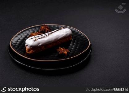 Delicious fresh profiterole or eclair with chocolate on a black ceramic plate on a dark concrete background