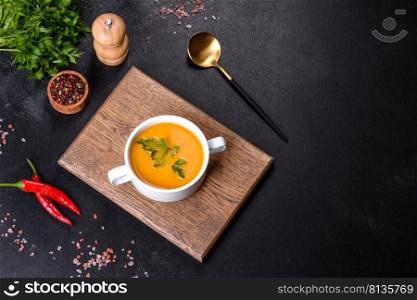 Delicious fresh pumpkin puree soup decorated with parsley in a white plate against a dark concrete background. Delicious fresh pumpkin puree soup decorated with parsley in a white plate