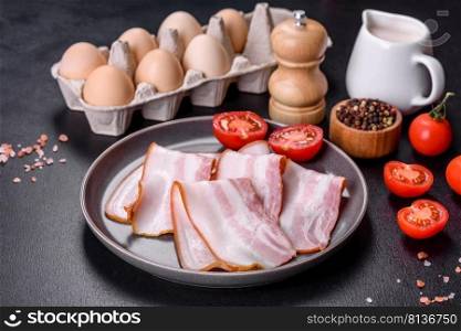 Delicious fresh raw bacon cut with slices on a grey plate against a dark concrete background. Making a delicious nutritious breakfast. Delicious fresh raw bacon cut with slices on a grey plate against a dark concrete background
