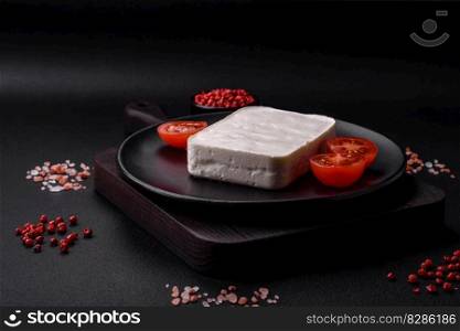 Delicious fresh rectangular shaped feta cheese with sπces and ve≥tab≤s on a dark concrete background