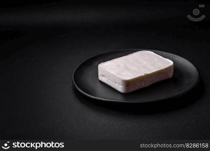 Delicious fresh rectangular shaped feta cheese with spices and vegetables on a dark concrete background