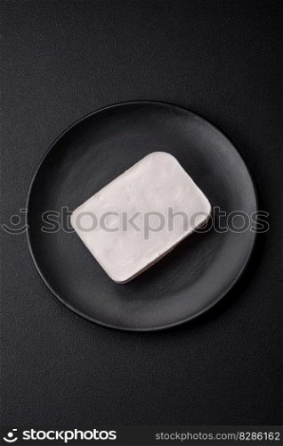 Delicious fresh rectangular shaped feta cheese with spices and vegetables on a dark concrete background