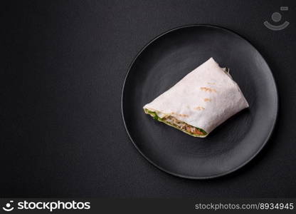 Delicious fresh roll with chicken, tomatoes, lettuce and cucumber in pita bread on a dark concrete background