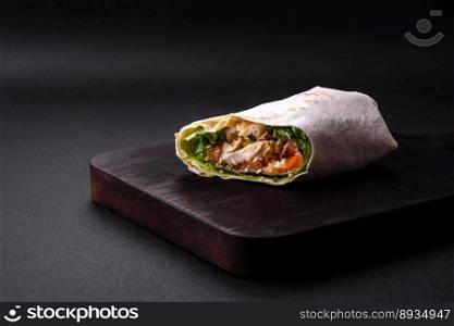 Delicious fresh roll with chicken, tomatoes, lettuce and cucumber in pita bread on a dark concrete background
