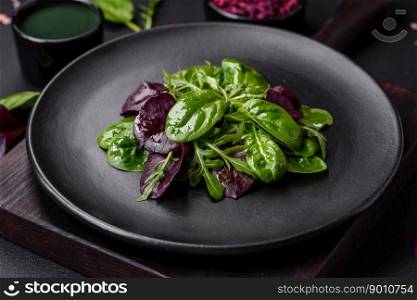 Delicious fresh salad consisting of spinach, chard, radicchio, red chart, bulls blood and arugula on a black plate on a dark concrete background