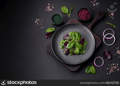 Delicious fresh salad consisting of spinach, chard, radicchio, red chart, bulls blood and arugula on a black plate on a dark concrete background