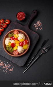 Delicious fresh salad of broccoli, cauliflower, sweet peppers and cherry tomatoes with spices and salt on a dark concrete background