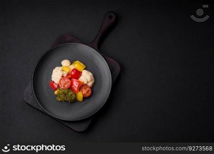 Delicious fresh salad of broccoli, cauliflower, sweet peppers and cherry tomatoes with spices and salt on a dark concrete background
