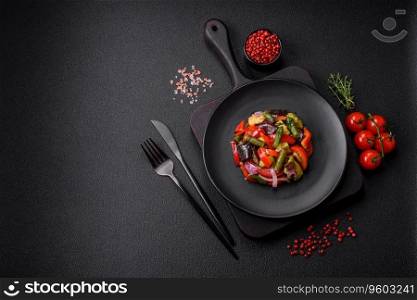 Delicious fresh salad of grilled vegetables peppers, tomatoes, eggplants and zucchini with salt and spices on a dark concrete background