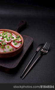 Delicious fresh salad of sliced   radishes with green onions, salt and olive oil on a dark concrete background