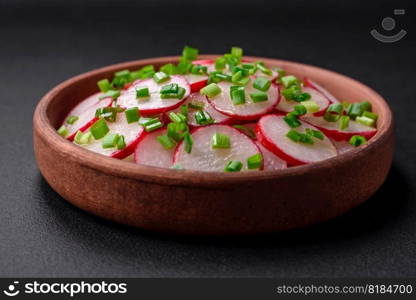 Delicious fresh salad of sliced   radishes with green onions, salt and olive oil on a dark concrete background