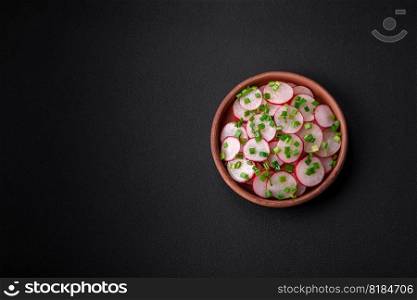 Delicious fresh salad of sliced   radishes with green onions, salt and olive oil on a dark concrete background