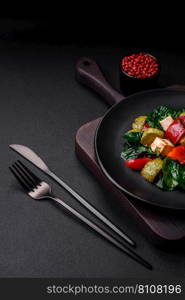 Delicious fresh salad of zucchini, cheese, sweet peppers, spinach with spices and herbs in a ceramic plate on a dark concrete background