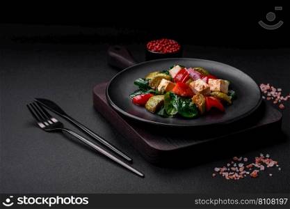 Delicious fresh salad of zucchini, cheese, sweet peppers, spinach with spices and herbs in a ceramic plate on a dark concrete background