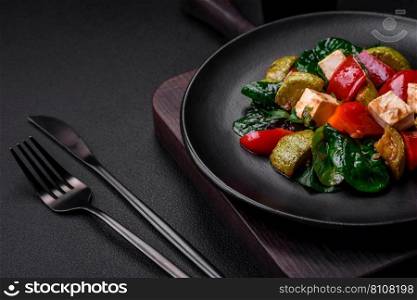 Delicious fresh salad of zucchini, cheese, sweet peppers, spinach with spices and herbs in a ceramic plate on a dark concrete background
