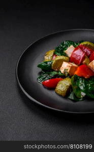 Delicious fresh salad of zucchini, cheese, sweet peppers, spinach with spices and herbs in a ceramic plate on a dark concrete background