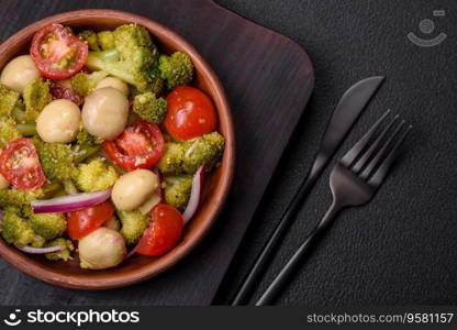 Delicious fresh salad with broccoli, cherry tomatoes, mushrooms, onions, salt, spices and herbs on a dark concrete background