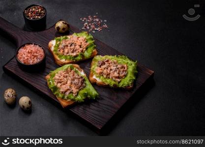 Delicious fresh sandwiches with toast, canned salmon, salad and quail eggs on a dark concrete background. Delicious fresh sandwiches with toast, canned salmon, salad and quail eggs