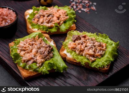 Delicious fresh sandwiches with toast, canned salmon, salad and quail eggs on a dark concrete background. Delicious fresh sandwiches with toast, canned salmon, salad and quail eggs