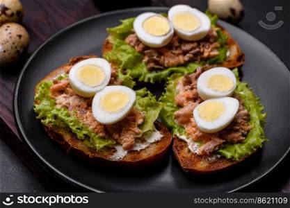 Delicious fresh sandwiches with toast, canned salmon, salad and quail eggs on a dark concrete background. Delicious fresh sandwiches with toast, canned salmon, salad and quail eggs