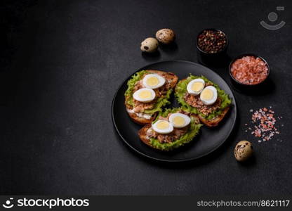 Delicious fresh sandwiches with toast, canned salmon, salad and quail eggs on a dark concrete background. Delicious fresh sandwiches with toast, canned salmon, salad and quail eggs