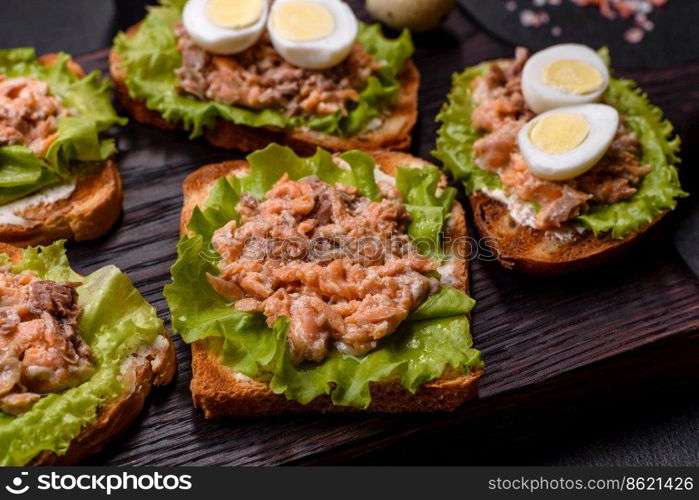 Delicious fresh sandwiches with toast, canned salmon, salad and quail eggs on a dark concrete background. Delicious fresh sandwiches with toast, canned salmon, salad and quail eggs