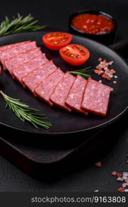 Delicious fresh sausage salami with salt, tomatoes and spices on a dark concrete background